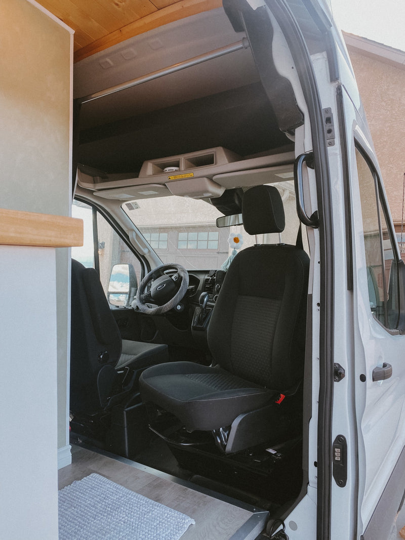 RV rental interior: The bright driver's cabin with black seats & Ford steering wheel, seen from the converted living space. — photo 11