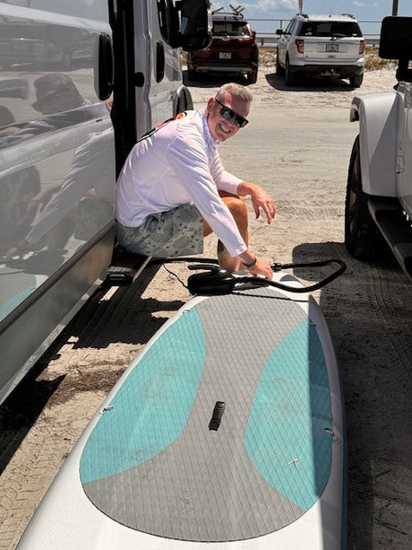 Smiling man inflates his paddleboard next to his RV rental, ready for adventure by the water.