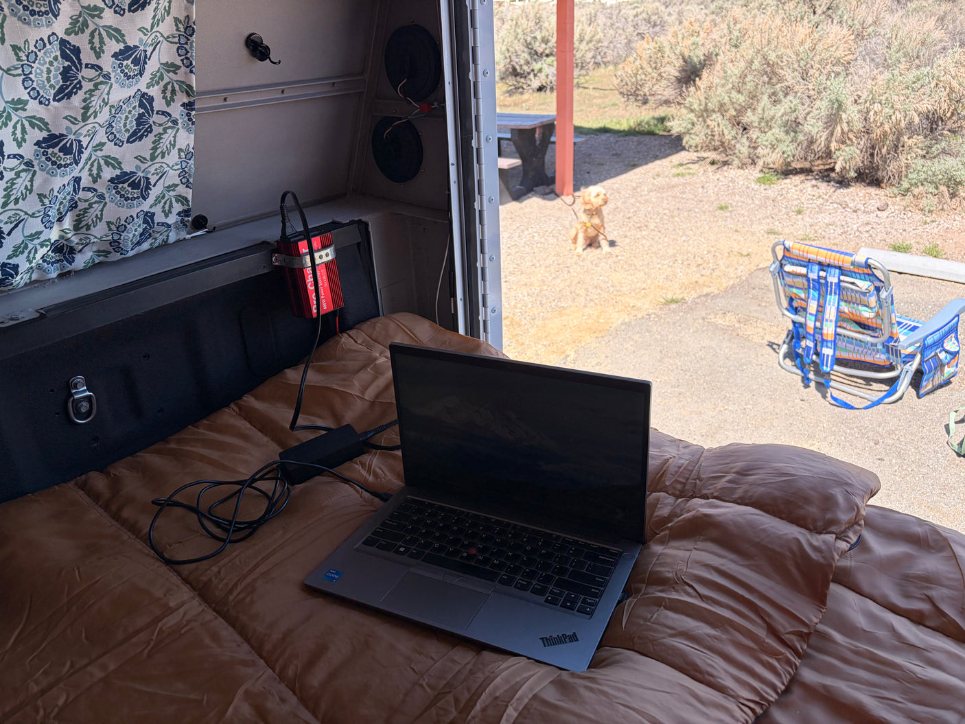 Working remotely from an RV rental: a laptop, power inverter, and a dog enjoying the outdoors. Perfect mobile office for travel.