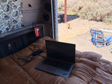 Working remotely from an RV rental: a laptop, power inverter, and a dog enjoying the outdoors. Perfect mobile office for travel.