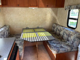 RV rental: Inside a camper, showing the dinette area with two patterned benches, table, and overhead storage.