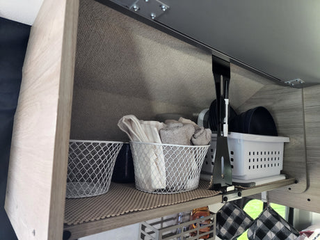 Organized RV rental cabinet with compact storage solutions: towels, dishes, and supplies in baskets & bins. Ideal for travel.