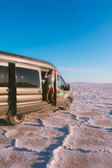 Explore vast landscapes! Woman steps out of her gray RV rental van onto salt flats under a clear sky.