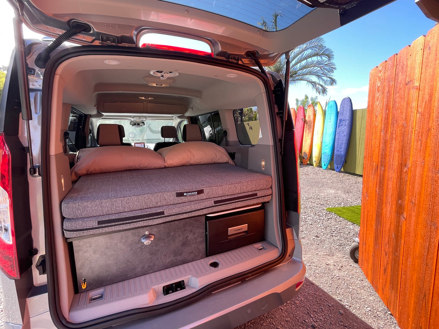 Compact camper van RV rental setup with cozy bed, storage, and fridge, perfect for surf adventures!