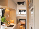 Inside an RV rental, a compact kitchen with a sink, plant, and cabinetry is seen next to a bunk bed with a ladder and ceiling AC.
