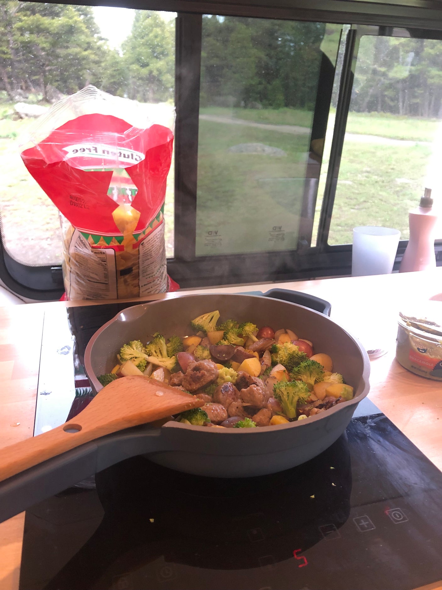 Cooking a hearty meal of meatballs, broccoli, and potatoes in an RV rental, with a scenic outdoor view.