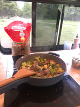 Cooking a hearty meal of meatballs, broccoli, and potatoes in an RV rental, with a scenic outdoor view.