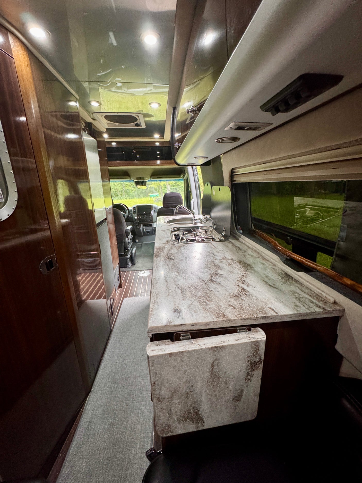 This RV rental offers a modern kitchenette with a sink, stove, and a marble-look counter, plus warm wood cabinetry inside.