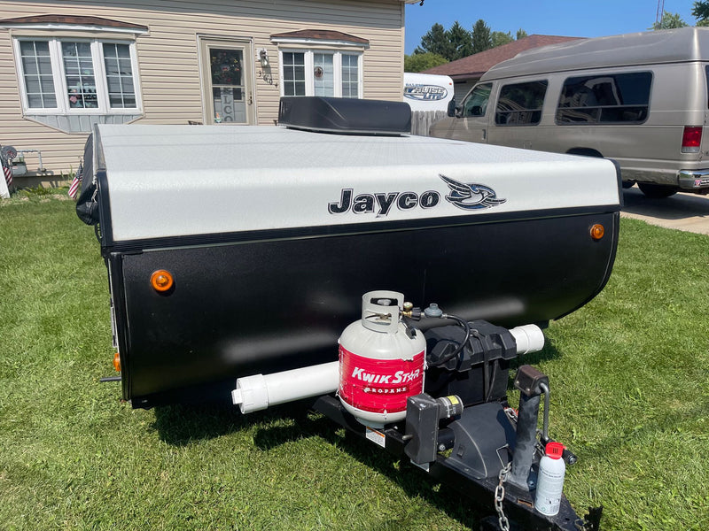 Jayco pop-up RV rental trailer, black and white with propane tank, parked on grass. A house and van are behind. — photo 7