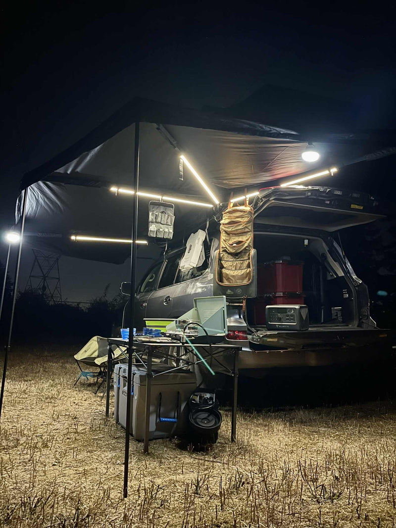 Night overlanding camp: SUV with lit awning, power station & gear in a field. Experience comfort, like an RV rental adventure. — photo 9