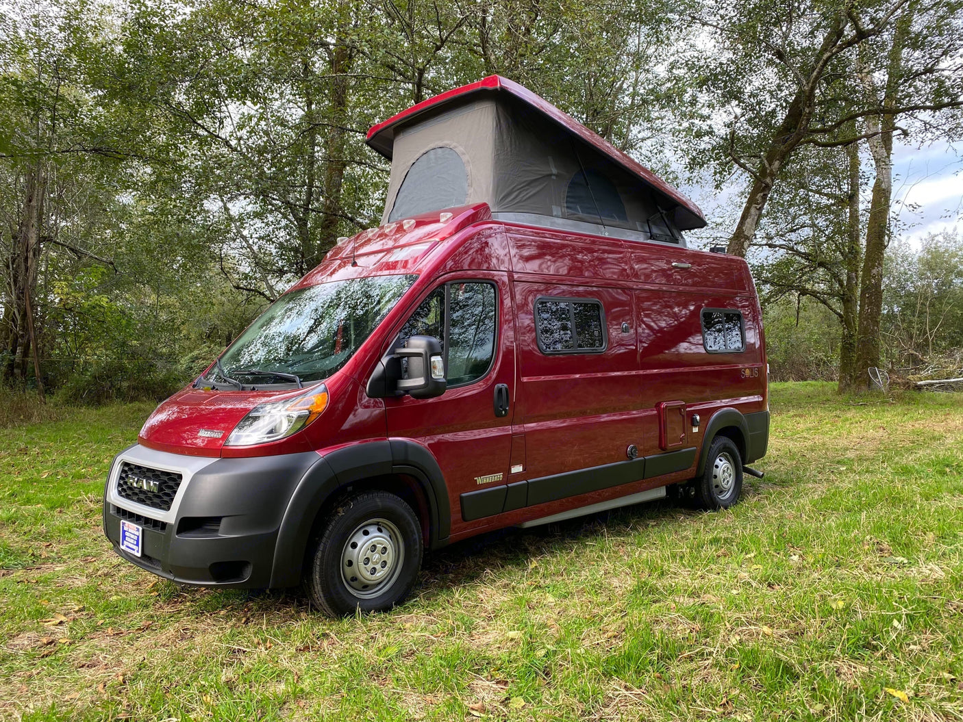 Red pop-top camper van for rv rental, parked on green grass among trees. This versatile camper is ready for adventure.