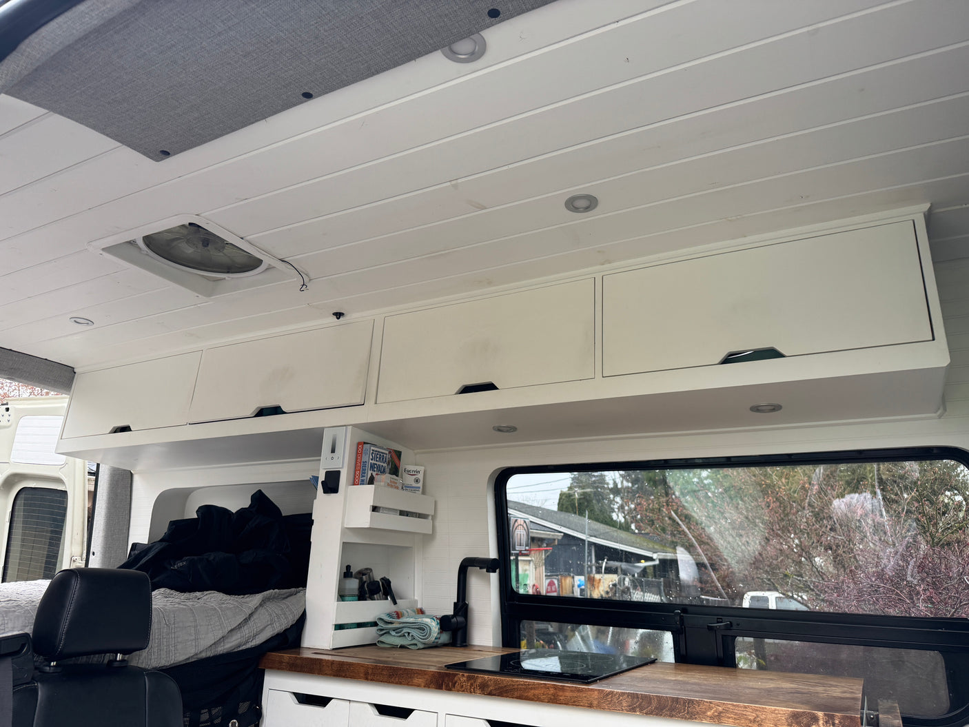 Spacious RV rental interior, showcasing a bright white ceiling, modern kitchen, cozy bed area, and overhead storage.