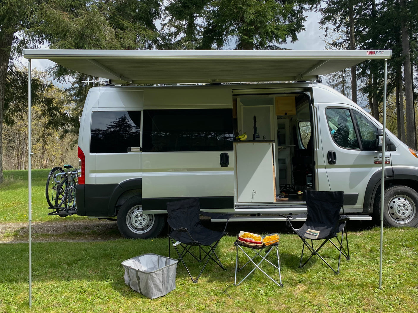 RV rental: White camper van with extended awning, chairs, and snacks outside. Bikes on the back for active outdoor adventures.
