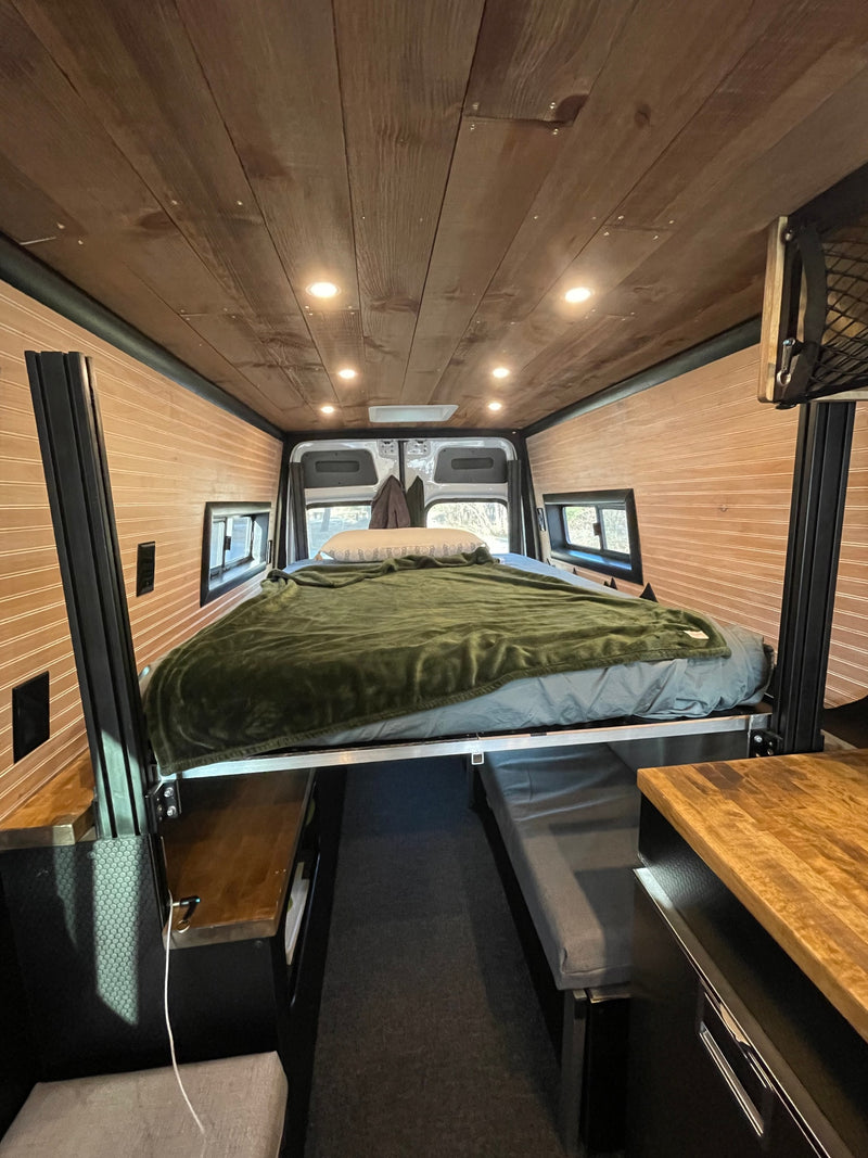 Inside a stylish RV rental, showcasing an elevated bed, wood-clad walls/ceiling, and a functional living space. — photo 6