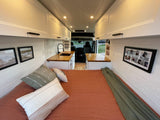 Cozy RV rental interior featuring a bed, kitchen, overhead cabinets, and stylish decor for mobile living.
