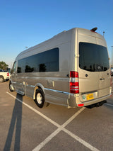 Golden Mercedes Sprinter RV rental, parked outdoors. Shows side profile, tinted windows, and rear with a peace sign sticker.
