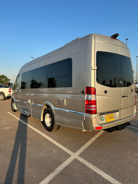 Golden Mercedes Sprinter RV rental, parked outdoors. Shows side profile, tinted windows, and rear with a peace sign sticker.