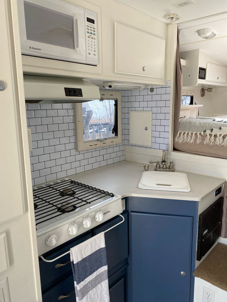 Modern RV rental kitchen with Dometic microwave, Suburban stove, sink, and blue cabinets, featuring subway tile backsplash.