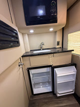 This rv rental features a well-equipped compact kitchenette with a microwave, sink, and open mini-fridge/freezer.