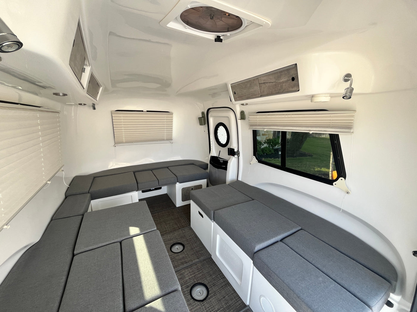 Modern RV rental interior with pristine white walls, grey convertible seating, overhead storage, and large windows. — photo 15