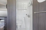 Inside an RV rental: a compact, white bathroom with toilet, sink, mirror, and towel bar for efficient living.