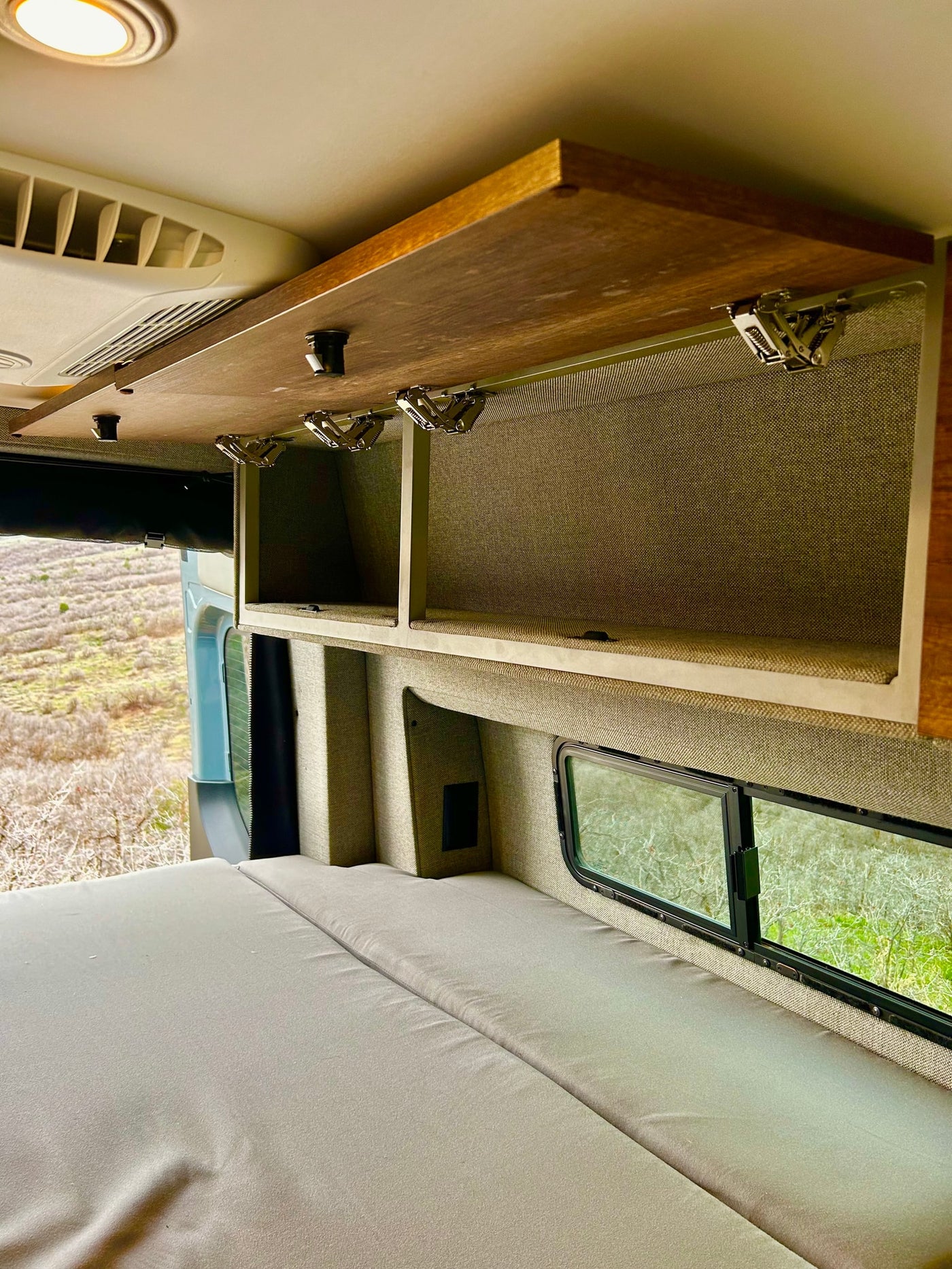 Interior of an RV rental: a comfortable bed, open overhead storage cabinet, and a window framing a natural landscape. — photo 20