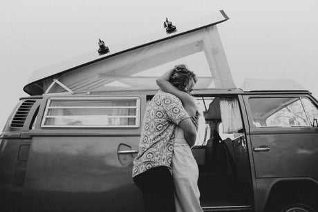 A couple shares a hug by a vintage pop-top VW camper in this grayscale image. Perfect for your next RV rental adventure.