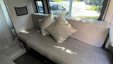 Cozy RV rental interior: grey sofa with floral pillows, window views, and a small storage net.