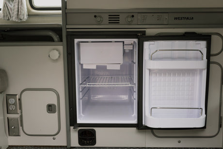 Spotless open RV rental refrigerator in a camper van interior, with controls visible. Perfect for your next road trip or camping adventure.