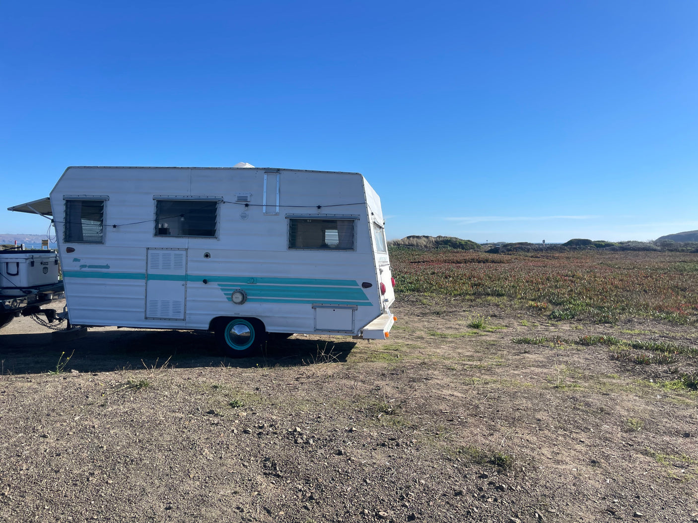 Vintage RV rental parked by a vibrant coastal field under a clear blue sky, perfect for outdoor adventures.