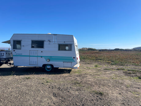 Vintage RV rental parked by a vibrant coastal field under a clear blue sky, perfect for outdoor adventures.