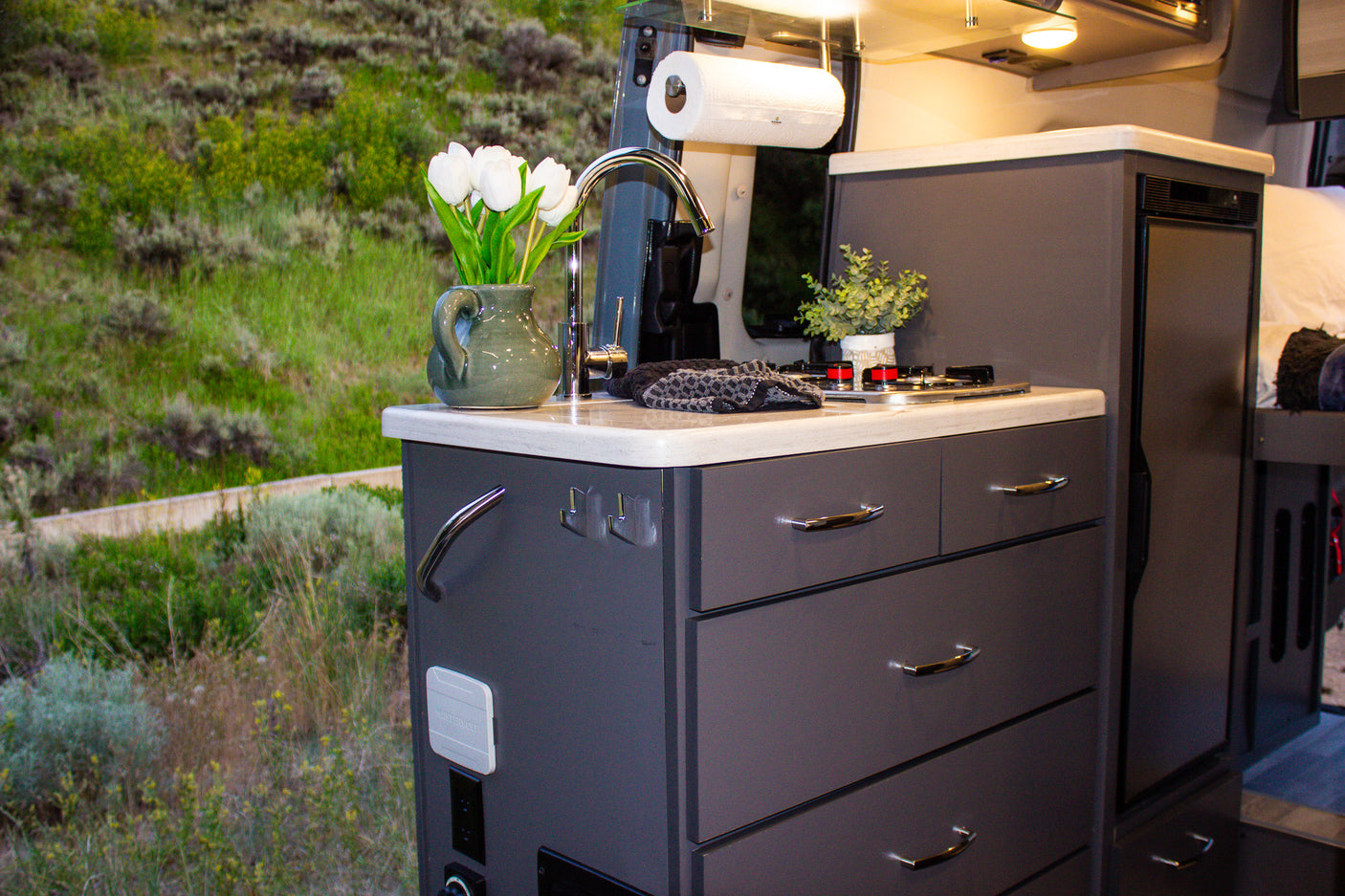 This rv rental features a modern, functional kitchen with a sink, stove, and ample storage, providing comfort amidst scenic outdoor views.