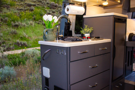 This rv rental features a modern, functional kitchen with a sink, stove, and ample storage, providing comfort amidst scenic outdoor views.