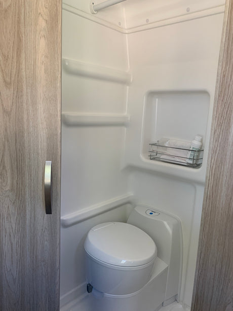 This RV rental features a clean, compact wet bath with a toilet, shower, and essentials on a built-in shelf.