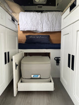 RV rental interior: Bed, white cabinets, and a pull-out portable toilet. Compact, functional design for life on the road.