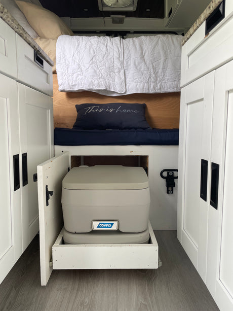RV rental interior: Bed, white cabinets, and a pull-out portable toilet. Compact, functional design for life on the road.