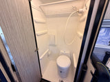 A compact, all-in-one wet bath in an RV rental, featuring a toilet, handheld showerhead, and small shelves within the shower stall.