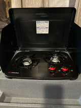 Two-burner Suburban propane stove with safety notice, common in an RV rental for cooking. Knobs show 'light', 'high', 'off' settings.