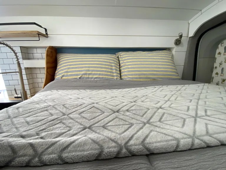 Cozy RV rental interior: bed with striped pillows & a plush blanket, compact kitchen, and cactus accents. — photo 20