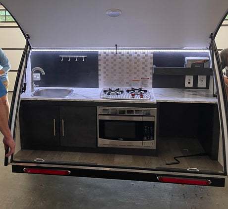 This RV rental features an open rear galley with a compact kitchen: sink, two-burner stove, microwave, and counter space.