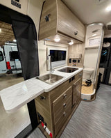 Modern rv rental camper van interior featuring a compact kitchen with sink, stovetop, and extendable counter, plus a wet bath with toilet.