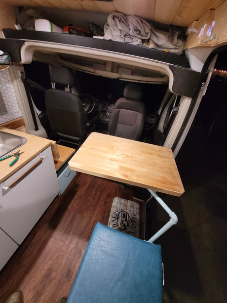 Inside an RV rental: a wood table/counter, sink, and front seats are visible, designed for compact van life.