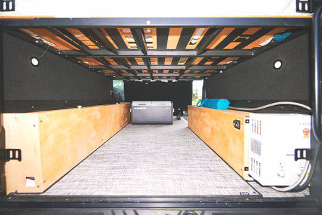 Spacious rv rental storage area with Dometic cooler, Excel water heater, and built-in wooden boxes under the bed frame.