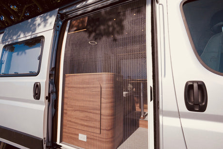 Step into comfort! This RV rental features a pleated mosquito net and a modern wooden interior, seen through its open side door.
