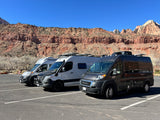 Three modern RV rental vans are parked in a scenic mountain area under a clear blue sky.