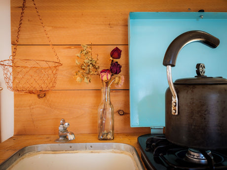RV rental kitchen: a small, wood-paneled space with a sink, dried flowers, and a kettle on the stove, perfect for compact living.