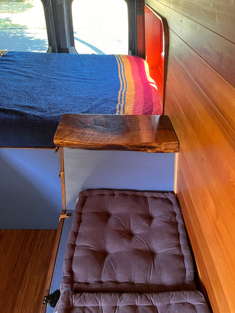 Inside this RV rental: a cozy custom wood interior with two sleeping areas, a colorful blanket, and natural light.