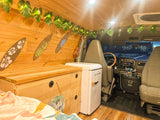 Step inside this cozy RV rental! Features wooden interior, tropical decor, a mini-fridge, and a comfy sleeping area.