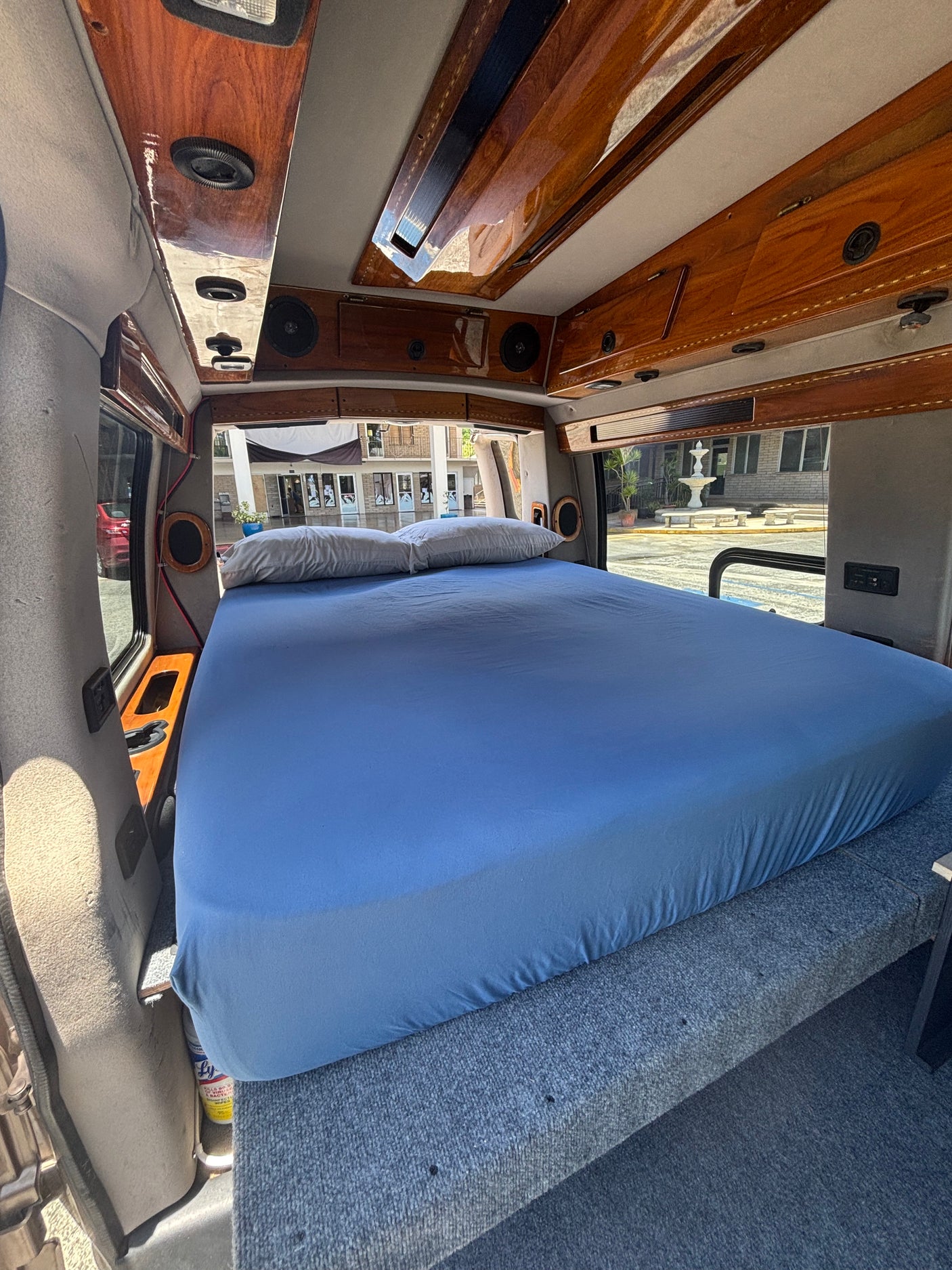 RV rental interior: A large bed with blue sheets, polished wood ceiling, and a fountain view outside.