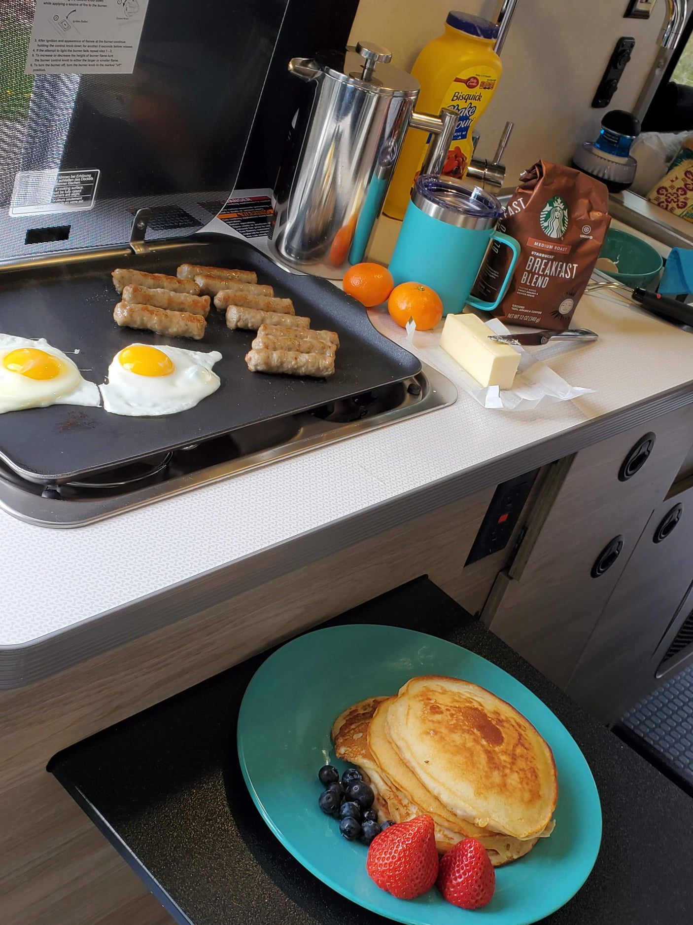 Breakfast is ready in this RV rental kitchen! Pancakes with fruit, eggs, sausages, and coffee make a perfect start to the day.
